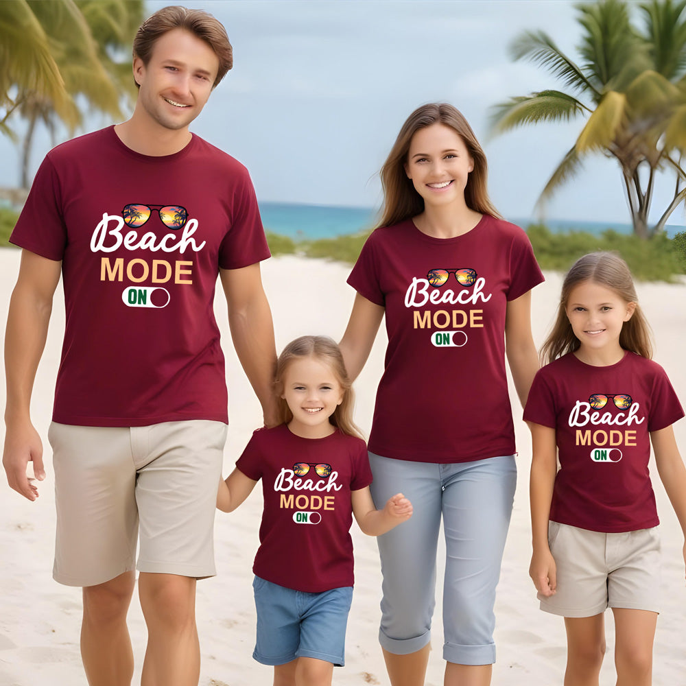 Family of four on a beach wearing matching 'Beach Mode ON' t-shirts.