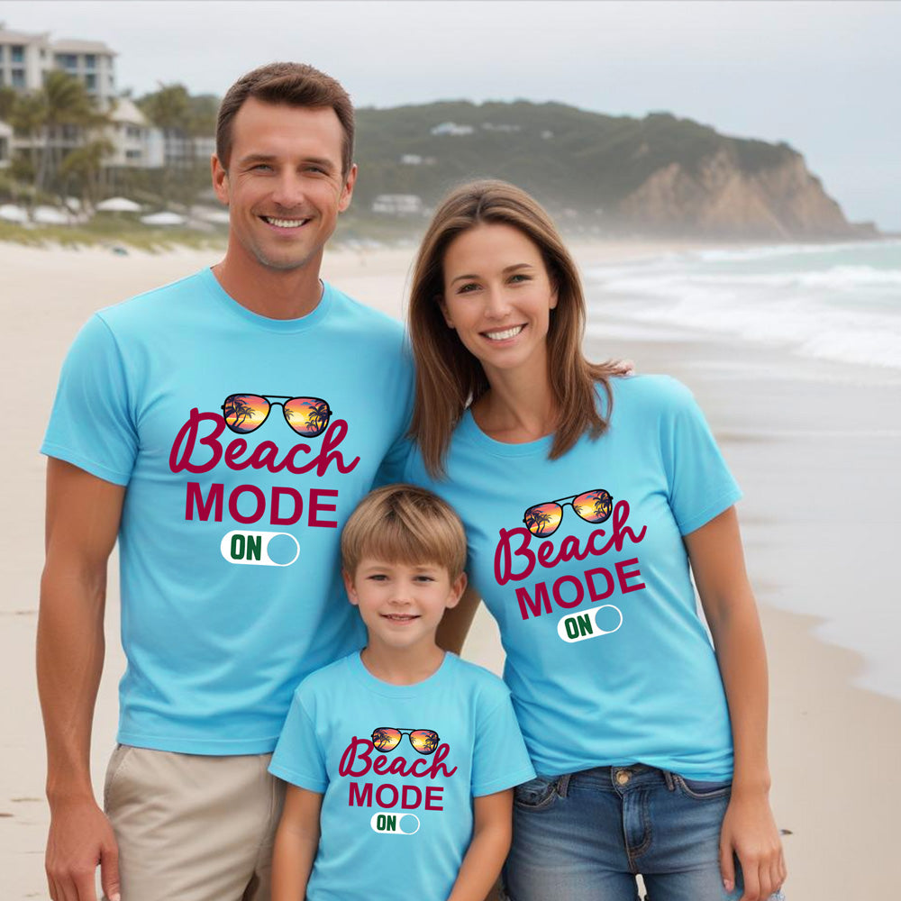 Family of three wearing matching blue t-shirts with 'Beach Mode ON' text on a beach.