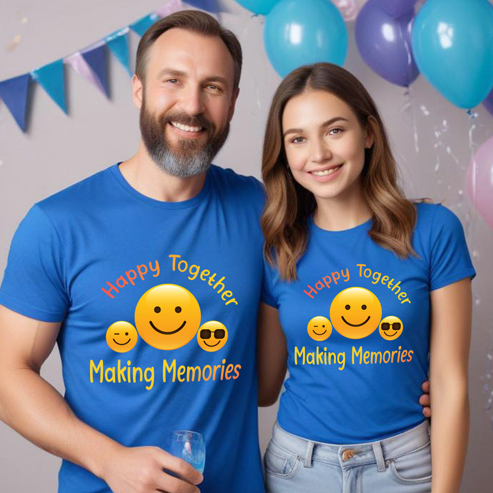 Man and woman wearing matching blue t-shirts with smiley faces and text, standing in front of balloons and a banner.