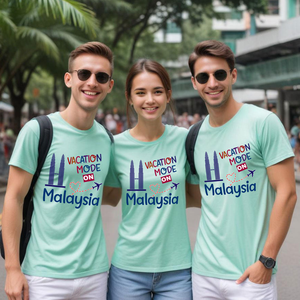 Three friends wearing matching light blue t-shirts with 'Vacation Mode ON Malaysia' text and graphics, standing outdoors.