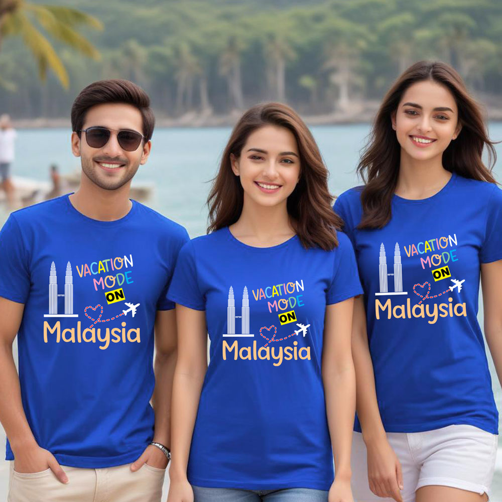 Three people wearing blue t-shirts with 'Vacation Mode ON Malaysia' text, standing by a scenic waterfront.