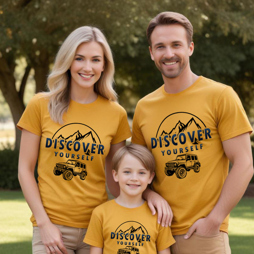 Family of three wearing matching yellow t-shirts with 'Discover Yourself' and jeep graphic outdoors.