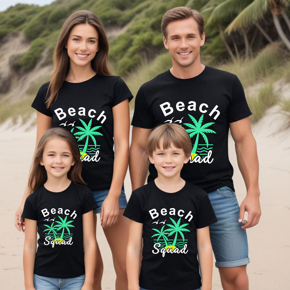 Family of four wearing matching black t-shirts with 'Beach Squad' text and palm tree graphics on a beach.