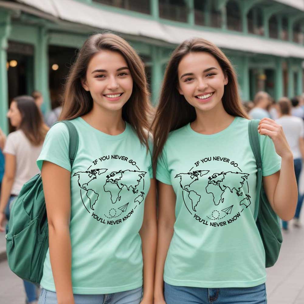 Two women wearing matching green t-shirts with a world map design in an urban setting.