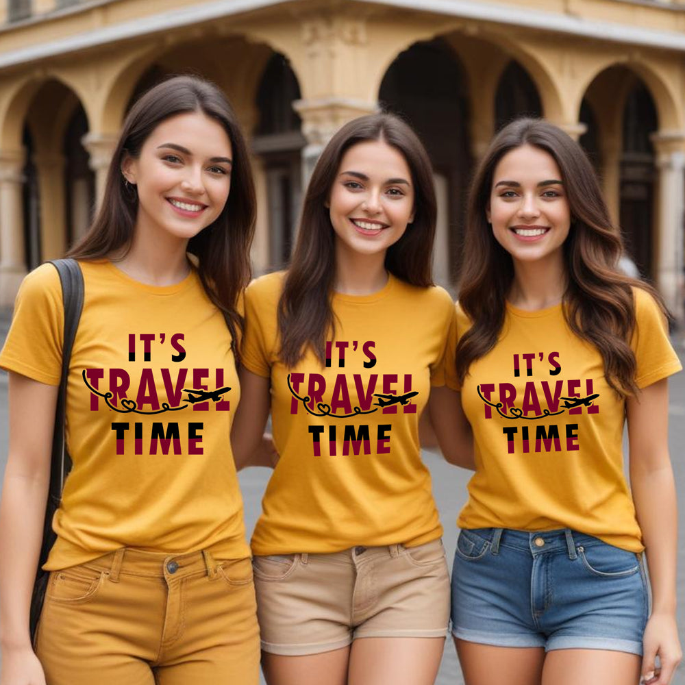 Three women wearing yellow t-shirts with 'It's Travel Time' text, standing in front of a building.