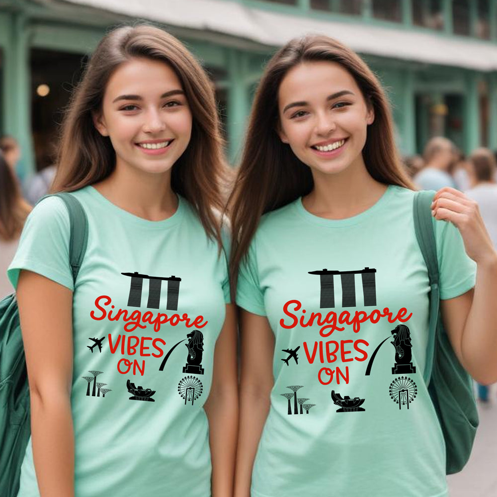 Two people wearing matching mint green t-shirts with 'Singapore Vibes On' text and graphics.