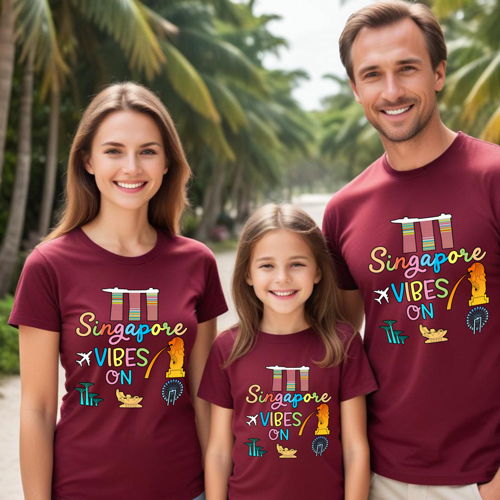 Family of three wearing maroon t-shirts with 'Singapore Vibes On' design outdoors.