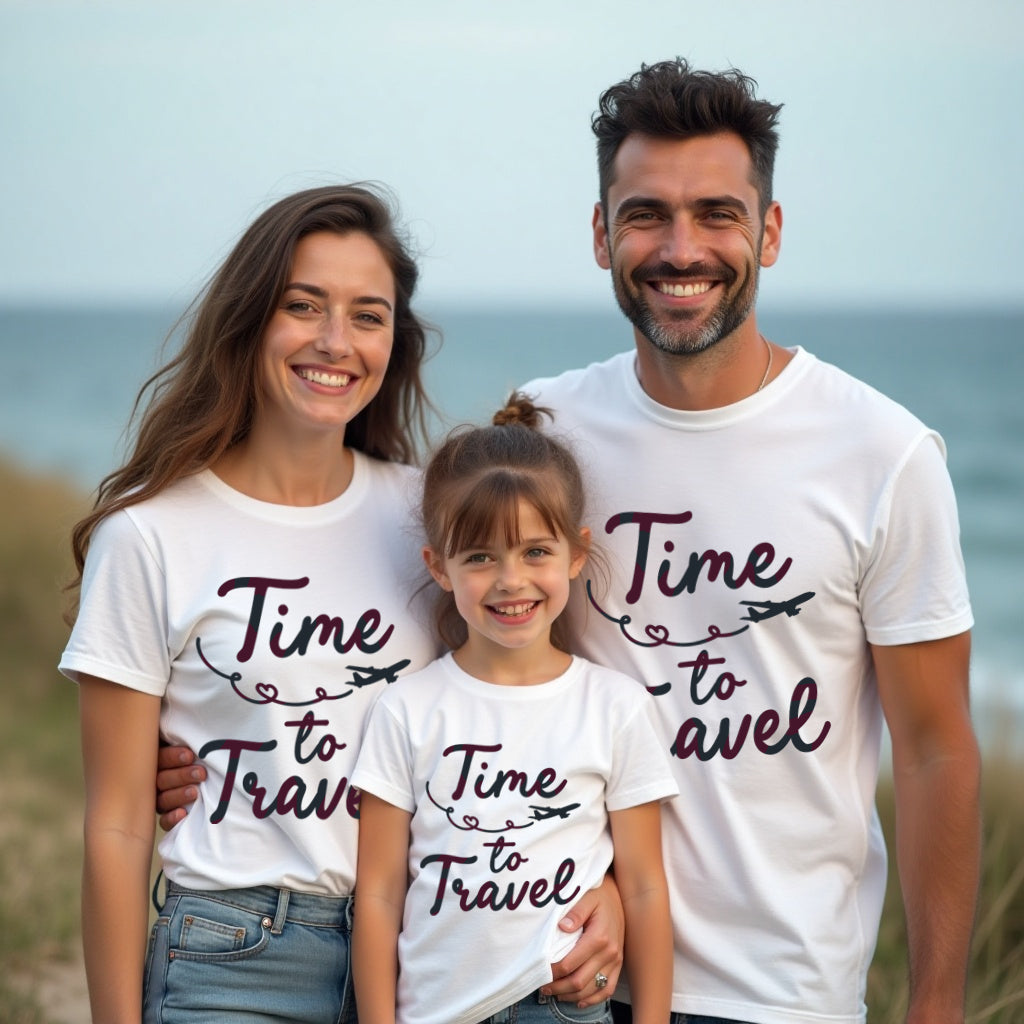 Family of three wearing matching 'Time to Travel' t-shirts by the ocean.